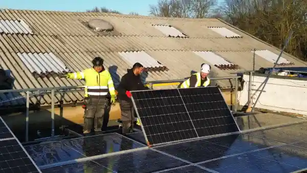 Electrical trainees installing solar panels on a flat roof during a practical training session, under clear blue skies. The system is part of a real-world 16kWh solar and battery installation project completed at the Learn Trade Skills training centre