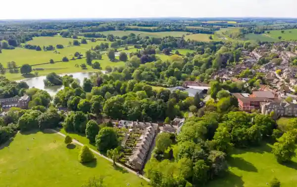 Aerial view of St Albans countryside showing a mix of green fields, tree-lined roads, a river, and residential housing nestled within lush greenery on a clear sunny day.