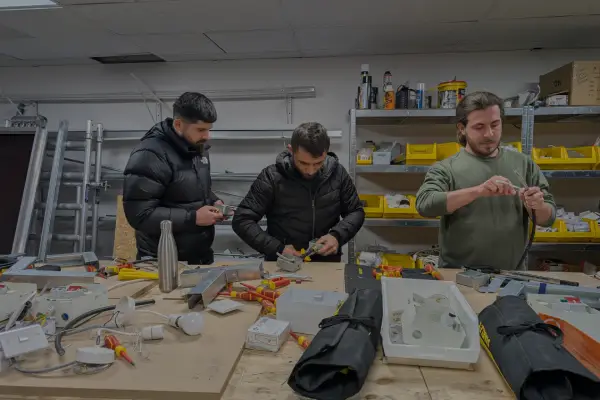 Electrical students in a UK training workshop practicing wiring and installation tasks with tools and components on the workbench.