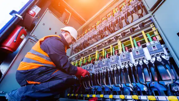 UK electrician in high-visibility safety gear working on industrial electrical panel, inspecting and maintaining circuits in compliance with 18th Edition Wiring Regulations