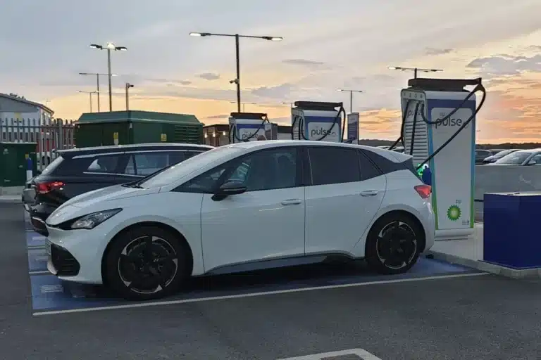 White electric car charging at a BP Pulse rapid charging station at sunset in a car park