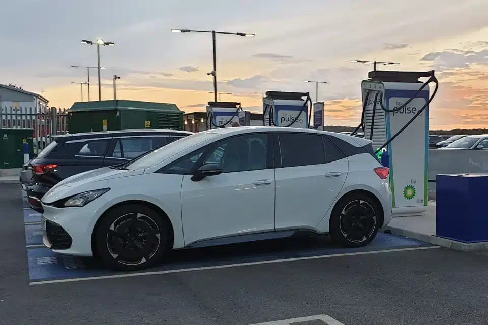 White electric car charging at a BP Pulse rapid charging station at sunset in a car park