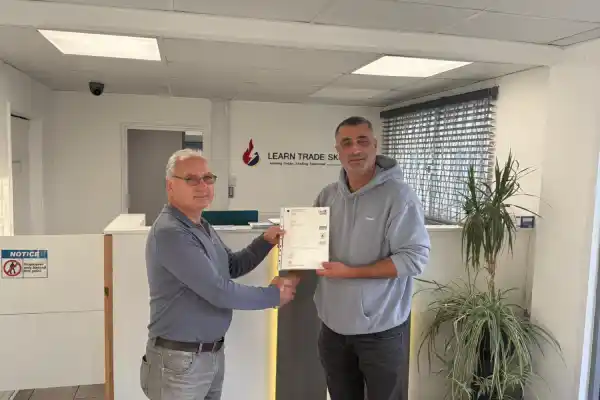 Learn Trade Skills instructor presenting a City & Guilds electrical qualification certificate to a newly qualified electrician at the Learn Trade Skills training centre in the UK.