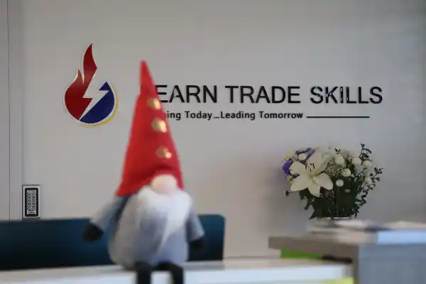 Reception area at Learn Trade Skills featuring the company logo on the wall, a festive gnome decoration in the foreground, and a bouquet of flowers placed on the desk.
